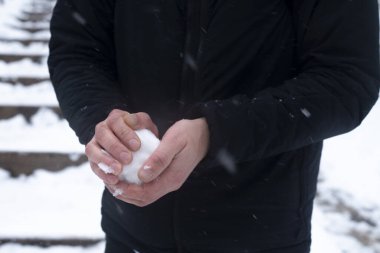 Bir erkeğin elindeki kartopu beyaz kar yığınlarının arka planına karşı.