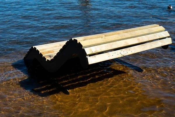 A wooden bench on a flooded embankment surrounded by water. — Stock Photo, Image