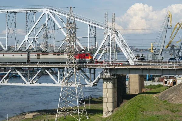 Bir elektrikli tren, sanayi şehrindeki bir nehirden geçen demiryolu köprüsünden geçiyor.. — Stok fotoğraf