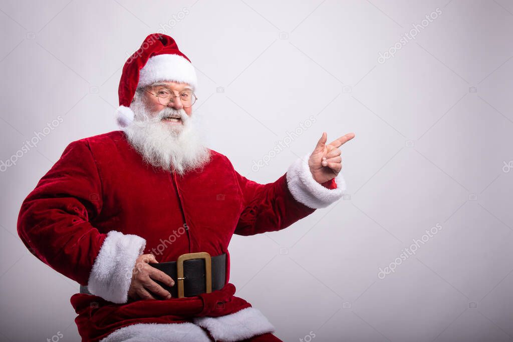 Happy Santa Claus, sat with hand in belt pointing a side in white background