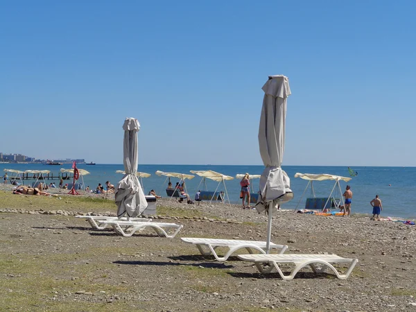 Beyaz güneşlikler ve şezlong, mavi deniz, insanlar Sahilde dinlenmek Soçi, Rusya — Stok fotoğraf