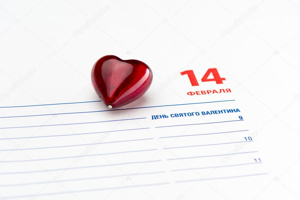 Red heart lies on a page of Diary. Diary is opened at 14 February page.  Text on the Diary page is written in russian and means 14 February,  st. Valentines day.