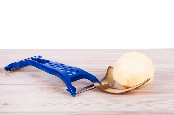 Potatoes, with a potato peeler — Stock Photo, Image