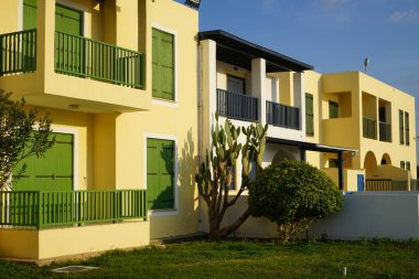 Yeşil ve siyah panjurlu iki katlı sarı bir ev.