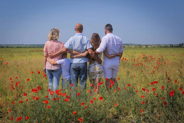 A family of five stands on a day in a poppy fieldwith their backs to the camera. friendly family, family reunification