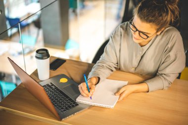 Bilgisayarıyla internetten okuyan, not defterine yazan bir kadın.