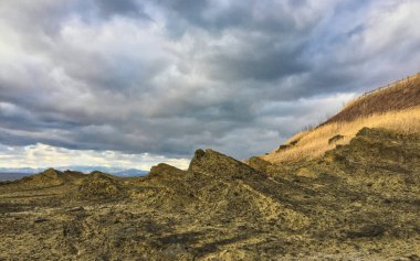 Pürüzlü, sarı volkanik kayalar mavi-gri bulutlu gökyüzüne karşı kurulmuş.