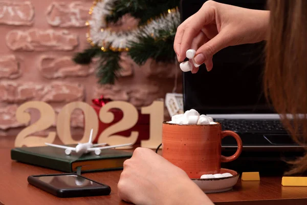 Adding marshmallows to a Cup of cocoa. The background is blurred with Christmas decorations and numbers 2021