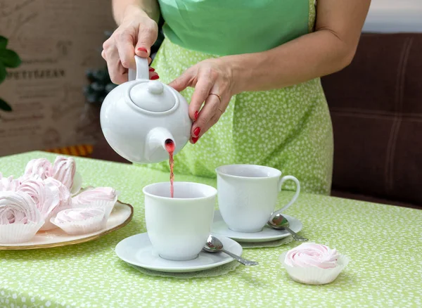 In a white mug, pour tea for a tea party with marshmallows. Selective focus.