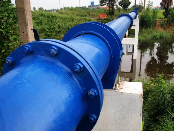 Eski boruları direkte tutmak için kıskaçlar ve fındıklar. Su kanalında yeşil bitkilerle beton bir kolon tabanındaki boruları birbirine bağlayan kıskaçlı ve cıvatalı mavi bir ana su borusu. Seçici odak