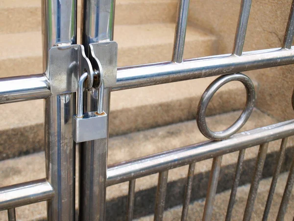 Kapı gümüş bir asma kilitle kilitli. Paslanmaz çelik kapı ızgaraları güvenlik veya hırsızlık koruması için kilitlidir. Kahverengi beton merdivenlerin arkasında. Seçici odak