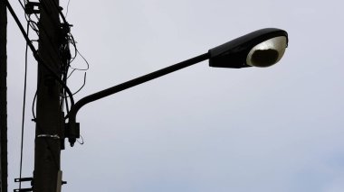 Sokak lambası silueti direğin üzerinde. Sokak lambası birçok ölü böcekle kaplı açık hava camını aydınlatır. Arka planda gökyüzü loş. Odaklan ve bir nesne seç