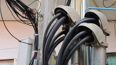 Servis giriş kapısında kablo var. Beton elektrik direğinin yanında galvanize metal boru var. Arka planda beton kolonlar ve duvarlar var. Odaklan ve bir nesne seç