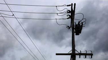 Saptırıcı silueti ve direklerde kablolar var. Üç aşamalı transformatörlü yüksek gerilim hattı ve arka planda elektriği dönüştürmek için fitil, fırtınanın kara bulutları var. Seçici odak