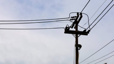 Yüksek voltajlı kabloların silueti ve kutuplardaki bağlantılar. Beton kutup destekli iletim hattı ve loş gri gökyüzü arkaplanı fotokopi alanı. Seçici odak