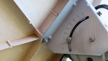 Uydu alıcısı yerleştirme derecesi. Dereceleri ayarlamak ve konumlandırmak için kullanılan bir metal, fotokopi alanı olan krem renkli bir uydu çanağının arkasında. Odaklan ve bir nesne seç