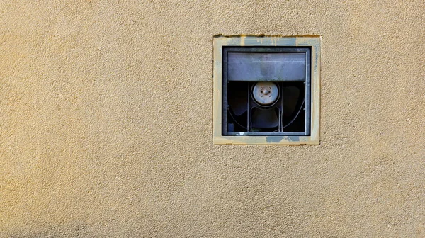 An old ventilation fan on the wall. The cream colored walls of the building have a dirty old exhaust fan with a copy space. Close focus and select an object