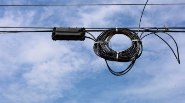 Kablolarda asılı fiber optik kablo rulosu. Fiber optik kablo açık havada yüksek hızlı internet iletişim sistemini destekliyor. Mavi gökyüzü arka planında ve kopyalama alanında. Seçici odak