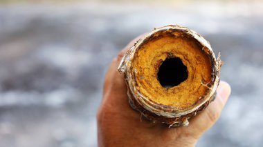 Old water pipes clogged. Man's hands held corroded metal plumbing and blocked the passage of water with rust forming inside the pipe. On a cement patio background with a copy space. Selective focus clipart