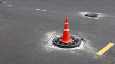 Ana delikte turuncu trafik konisi. Asfaltlı bir yolda yeni bir kanalizasyon borusunun döşenmesi ile ilgili trafik işaretleri. İçeriği seçin ve odağı kapatın.