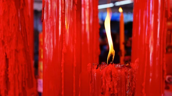A burning red candle and a yellow flame. Several large red candles were lit in the shrine of the Thai people of Chinese descent. Selective focus