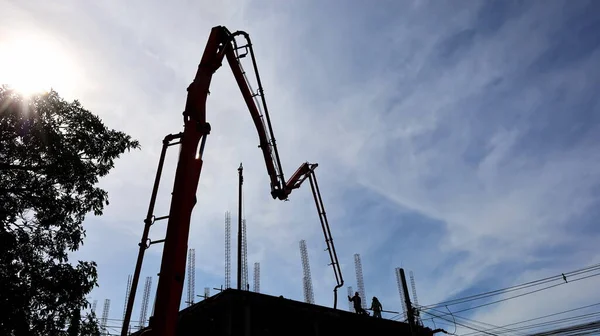 Silhouette of a concrete pump boom. Machinery to pump the concrete on the top of the building at the construction site On the sky background there are white clouds with copy space. Selective focus