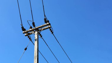 Direkte yüksek voltaj kabloları var. Güç iletim hattı ve beton kutuplarda fotokopi alanı olan mavi gökyüzü arka planına karşı destek. Seçici odak