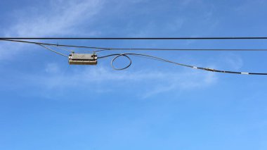 Kablolara siyah bir plastik kutu asılmış. Yüksek hızlı internetin fiber optik dağıtıcısı için fiber optik ayırıcı (Plc, Coupler). Fotokopi alanı olan mavi bir gökyüzü arka planında. Seçici odak