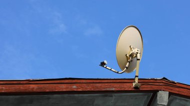 Çatıda uydu anteni var. Beyaz metal çanak anten ve TV alıcısı uydu teknolojisiyle haberleri izlemeye gidiyor. Fotokopi alanı olan parlak mavi bir gökyüzü arka planında. İçeriği seç ve odaklan
