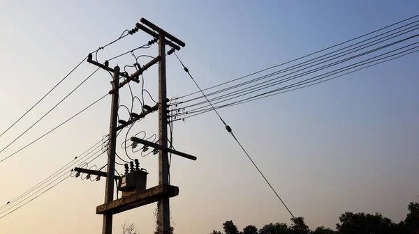 Silhouette of a transformer on a power pole. High voltage transmission lines and three-phase transformers for serving the community On the background of the sky with sunlight, dawn with copy space.