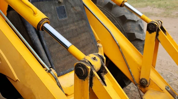 Eski kazıcının hidrolik silindiri. Zemin kattaki inşaat alanında sarı ağır ekipman kolunda hidrolik silindir ve krom pistonlar var. Seçici odak