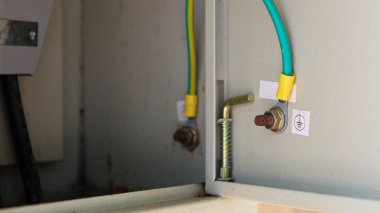 Metal bir kutunun içindeki kabloyu kapat. Gri şalter kutusunda yeşil ve sarı bir kablo var. Kutunun kapağında zemin sembolü etiketi olan kısa bir devreyi önlemek için..