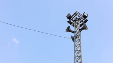 Sahne ışıkları direğinde korna hoparlörleri. Yayın sistemi halkı mavi gökyüzü arka planında bilgilendiriyor. Odaklan ve bir nesne seç