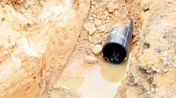 Delikte su tesisatı var. Siyah plastik boru (HDPE) üreme alanı olan bir köy su tedarik sisteminin yapımı sırasında toprak çukuruna gömüldü. Seçici odak