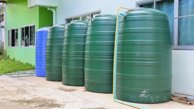Saflar dolusu yeşil su tankı. Evin yanındaki çimento zeminde yeşil ve mavi plastik kovalar. Acil su deposu için fotokopi alanı var. Seçici odak