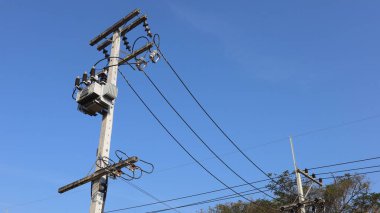 Transformatörde. Yüksek voltaj kablolarına ve mavi gökyüzü arkaplanındaki beton kutuptaki sigorta sistemine sahip 3 fazlı elektrik trafosu ve seçici odaklı kopyalama alanı.