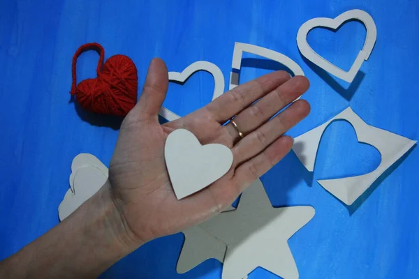 Make a star and heart out of cardboard and yarn. Blue background. Heart in hand