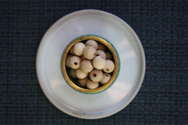 Gri arka planda cam bir tabakta tahta boncuklar..