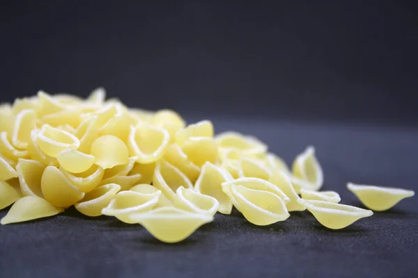 Small pasta in the form of seashells on a black background. Space for text.