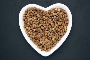 Siyah arka planda kalp şeklinde bir kasede karabuğday. Metin için boşluk.