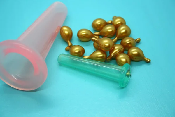 A jar for facial massage and gold capsules with oil. Blue background.