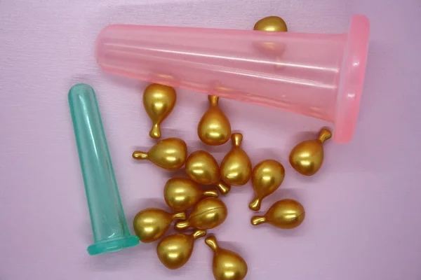 A jar for facial massage and gold capsules with oil. Pink background.