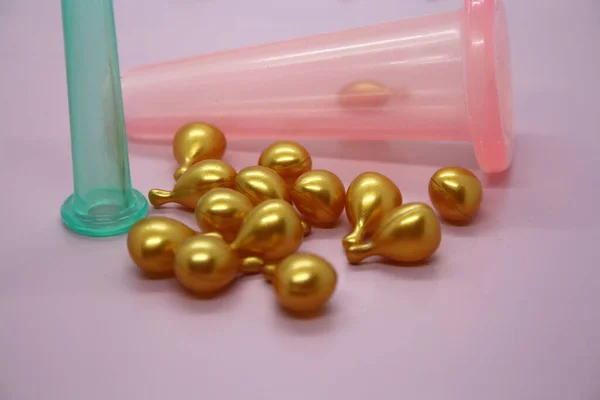 A jar for facial massage and gold capsules with oil. Pink background.