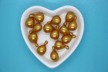 Kapsül altın yağı, kalp şeklinde beyaz tabakta yüz için. Mavi arkaplan.