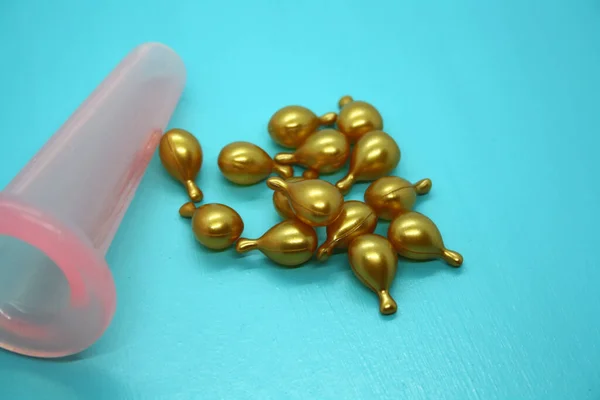 A jar for facial massage and gold capsules with oil. Blue background.