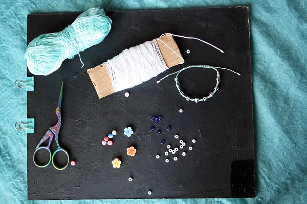 Materials for making a bracelet from beads and threads. Space for text.