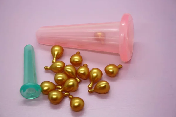 A jar for facial massage and gold capsules with oil. Pink background.