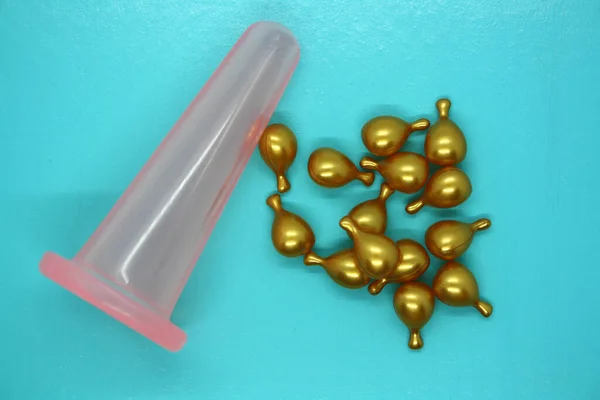 A jar for facial massage and gold capsules with oil. Blue background.