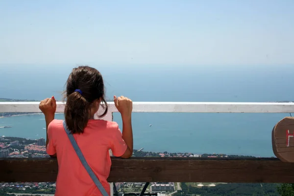 A girl looks at the sea from an observation deck in the mountains.