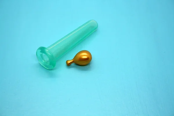 A jar for facial massage and gold capsules with oil. Blue background.
